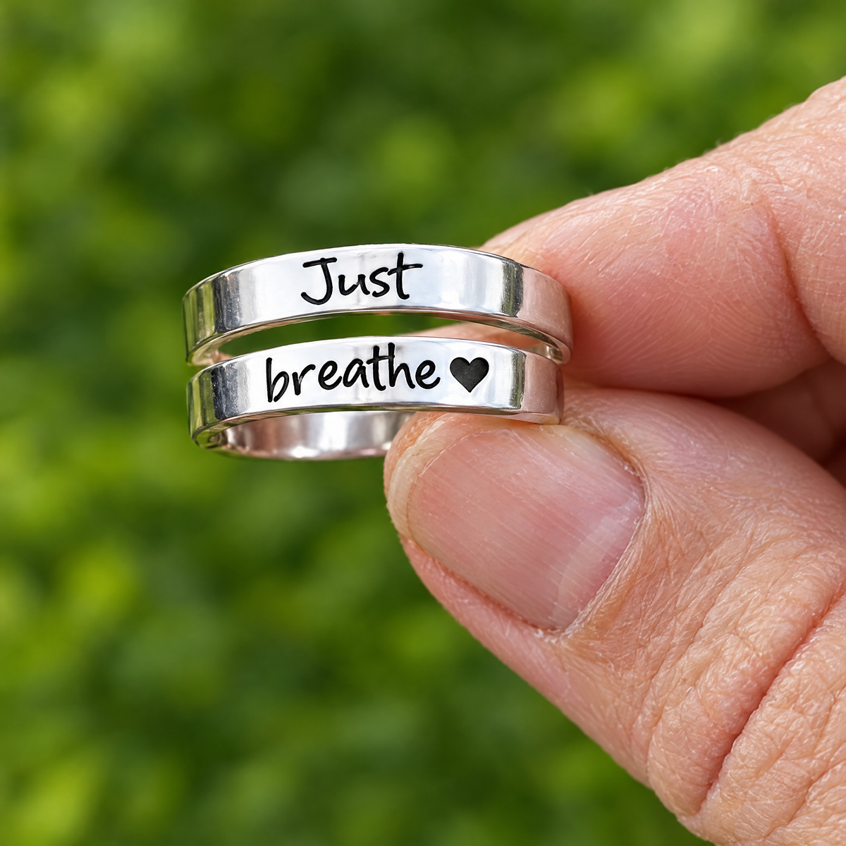 The Breathe Ring held up, stainless steel wrap with Just breathe and a heart